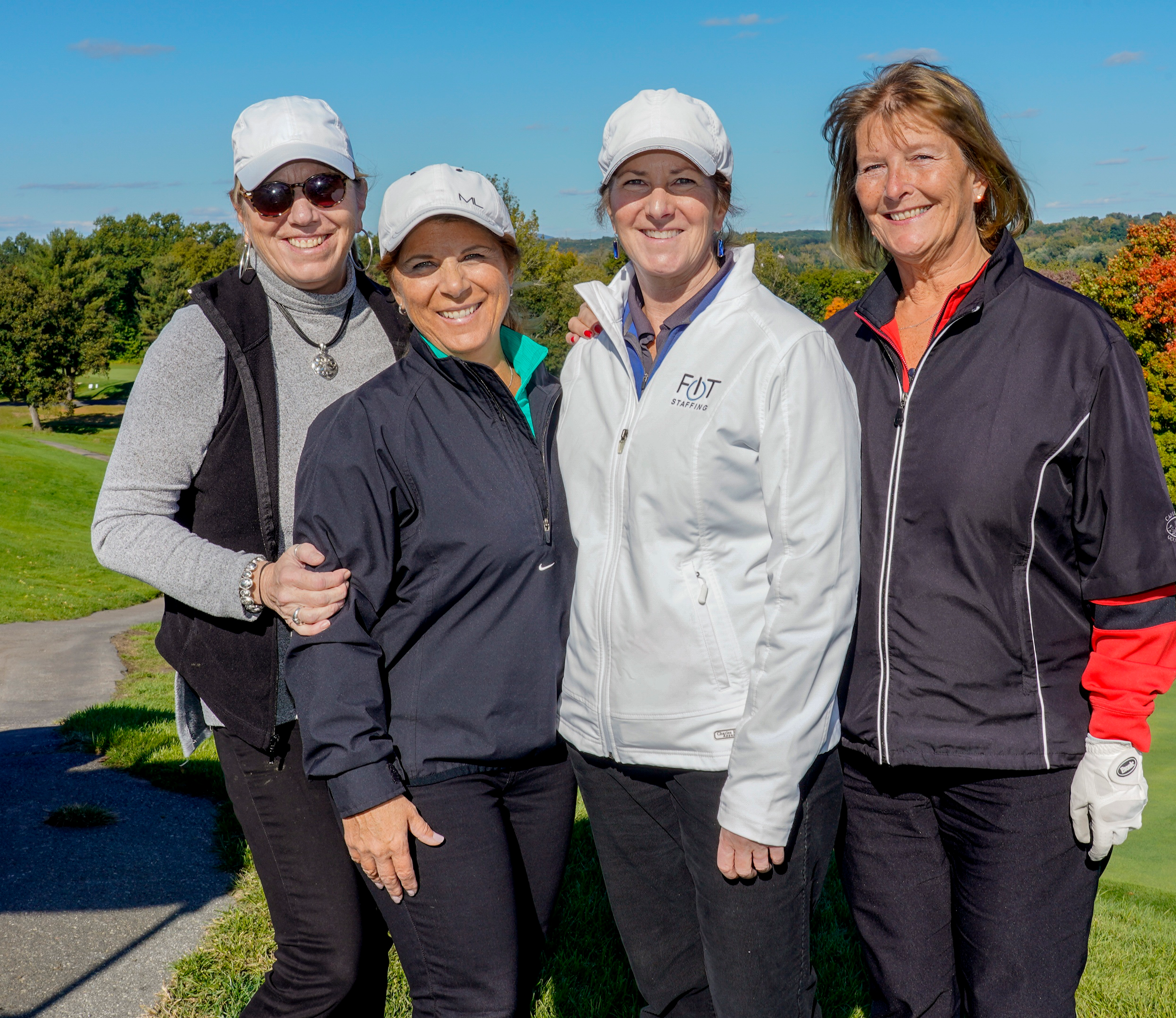 Four women stand, smiling, on a golf green. 